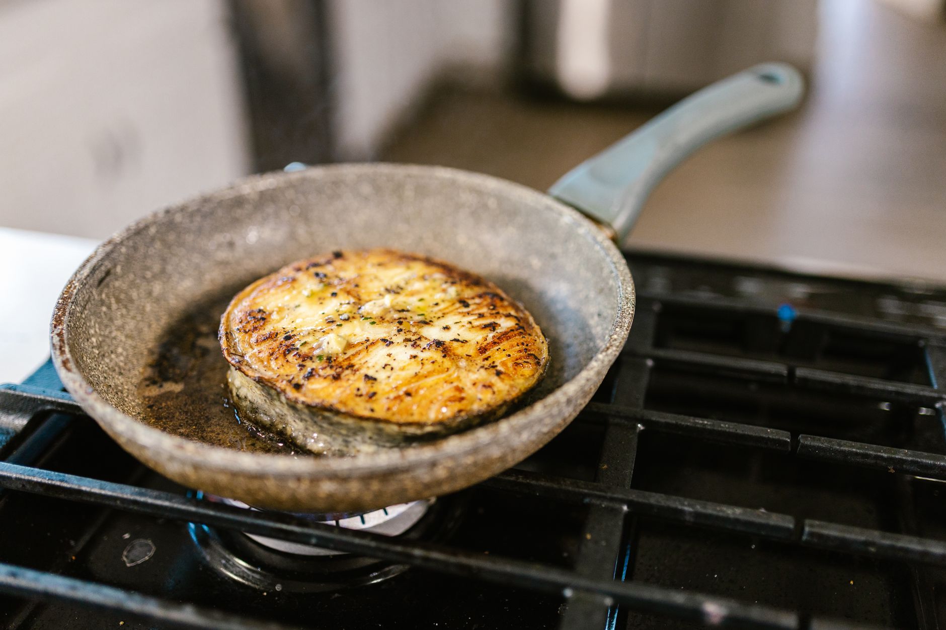 Close-up of a golden-brown salmon steak cooking in a frying pan on a gas stove.