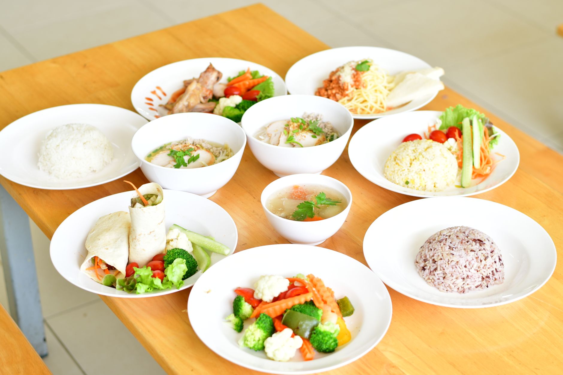 A variety of healthy dishes including rice, soup, and vegetables served on a wooden table.